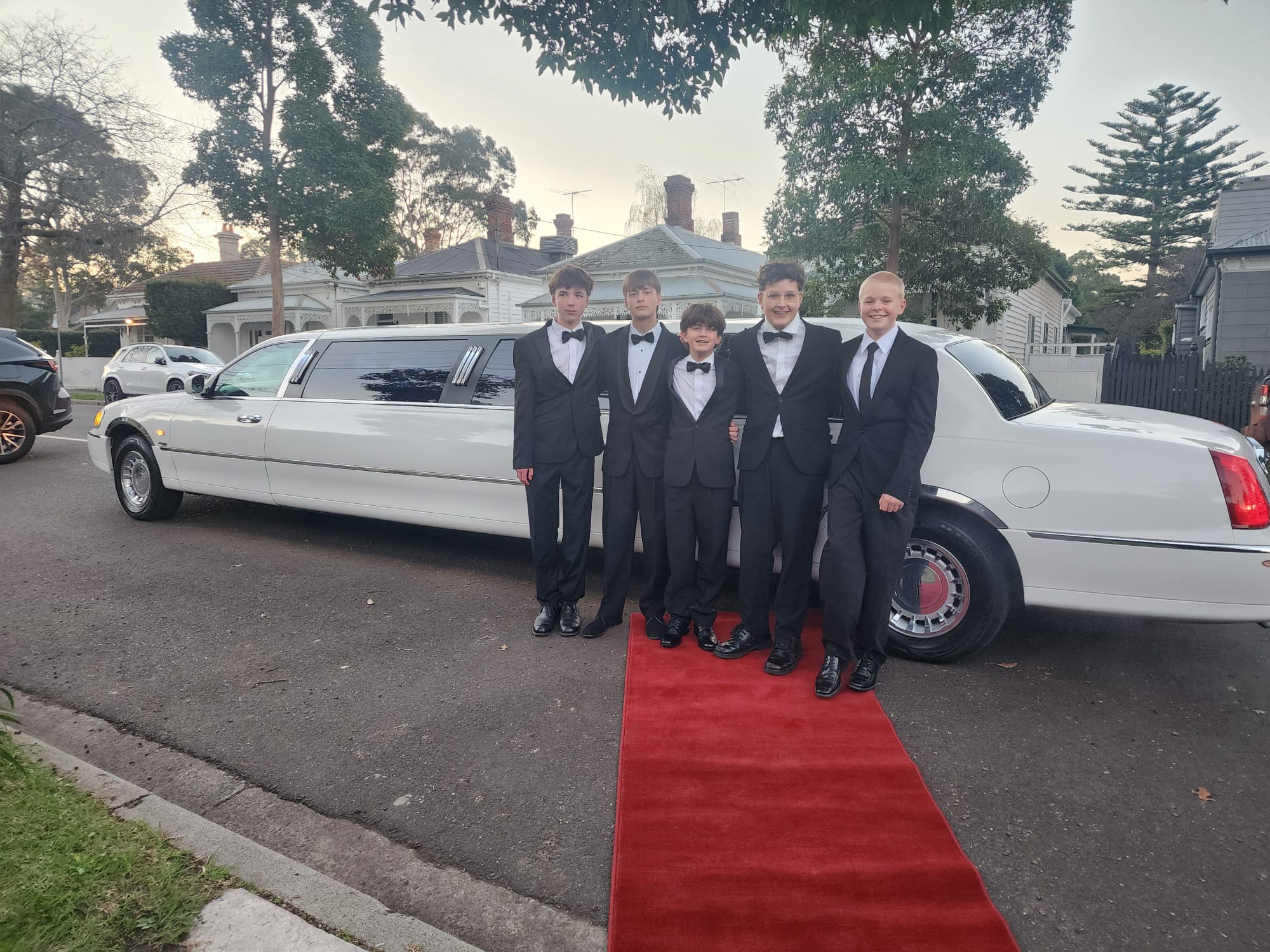 Group in formal suits on red carpet beside Auslink stretch limo, Melbourne
